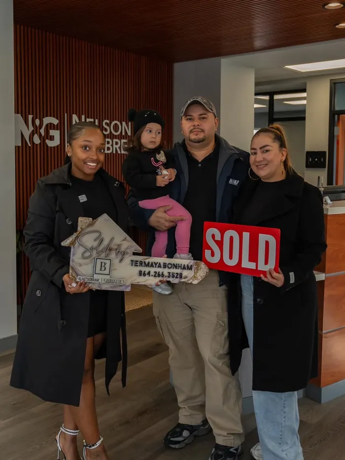 Helly and Karen&rsquo;s family holding a Sold sign at their closing